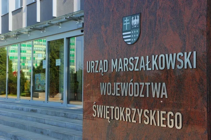 Wejście do siedziby Urzędu Marszałkowskiego Województwa Świętokrzyskiego z herbem regionu na ścianie z czerwonego granitu.