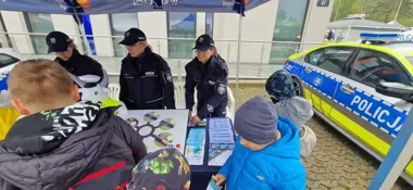 Policjantki rozmawiają z dziećmi przy stoisku edukacyjnym pod namiotem obok radiowozu.