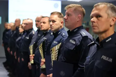 Funkcjonariusze polskiej policji w mundurach stoją w szeregu podczas uroczystości wręczenia nagród, trzymając statuetki i dyplomy.