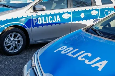 Dwa policyjne radiowozy oznaczone napisem „POLICJA” stoją na asfaltowej nawierzchni.