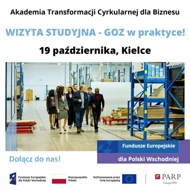 Grupa osób w odzieży biznesowej przechodzi między regałami w hali magazynowej lub produkcyjnej.