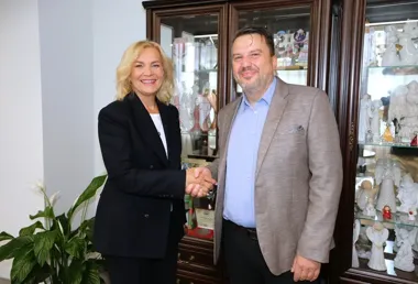 Kobieta w czarnym garniturze i mężczyzna w beżowej marynarce witają się uściskiem dłoni w pomieszczeniu biurowym z witryną z figurkami aniołów.