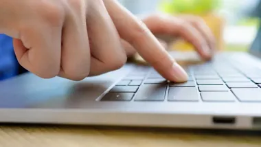 Dłonie osoby piszącej na klawiaturze laptopa.