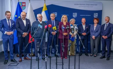 Grupa osób stoi podczas konferencji prasowej w siedzibie województwa świętokrzyskiego, przed mikrofonami mediów.