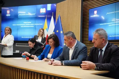W sali konferencyjnej w Kielcach odbywa się uroczyste podpisanie umowy o dofinansowanie szkolnej pracowni komputerowej, przy stole zasiadają cztery osoby, a w t