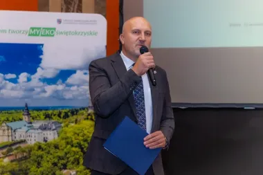 Mężczyzna w garniturze przemawia do mikrofonu podczas konferencji w Kielcach, w tle baner promujący EKO Świętokrzyskie.