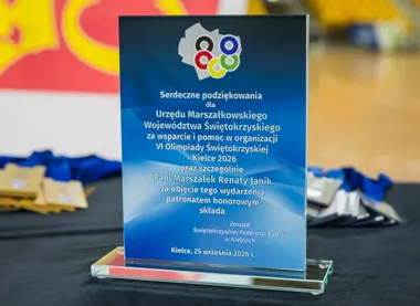 Szklana statuetka z podziękowaniami dla Urzędu Marszałkowskiego Województwa Świętokrzyskiego i marszałek Renaty Janik leży na czarnym stole z medalami w tle.