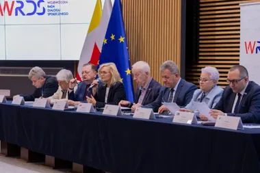 Uczestnicy panelu siedzą przy stole podczas posiedzenia Wojewódzkiej Rady Dialogu Społecznego, w tle flagi Polski i Unii Europejskiej oraz logo WRDS.