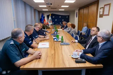 Spotkanie służb mundurowych i urzędników przy długim stole konferencyjnym w pomieszczeniu urzędowym.