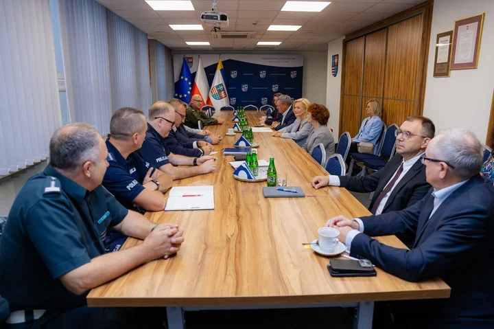 Spotkanie służb mundurowych i urzędników przy długim stole konferencyjnym w pomieszczeniu urzędowym.